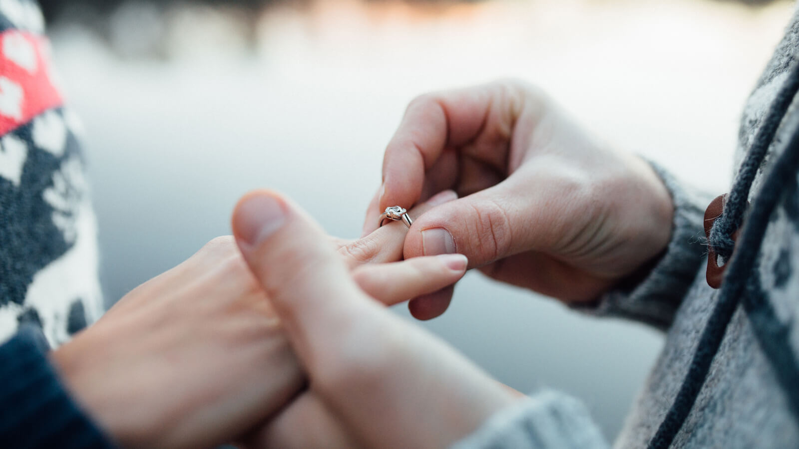 Picture of man putting engagement silver ring on woman hand, outdoor. Sea or river background.