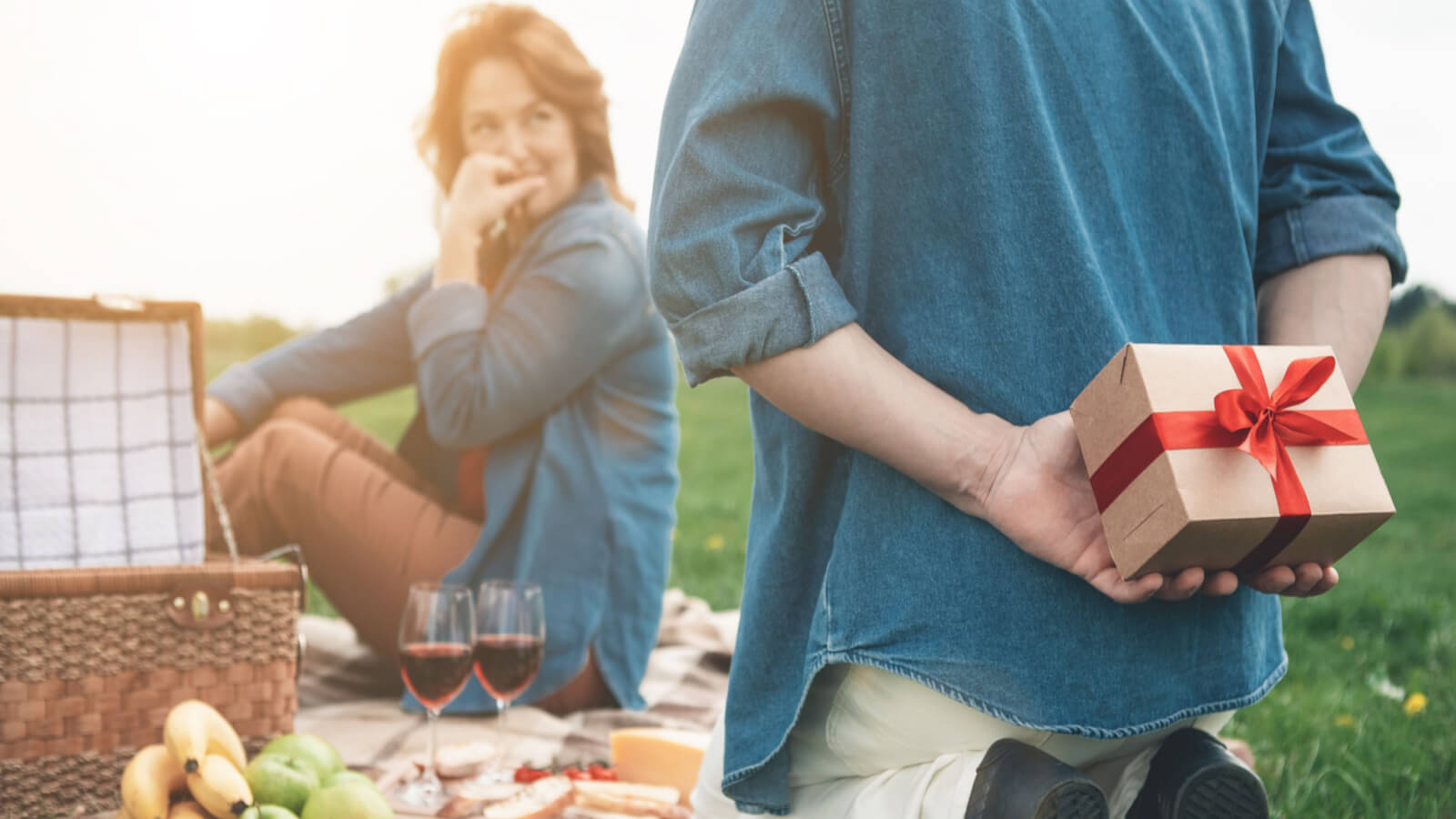 couple on picnic, man holding gift behind back