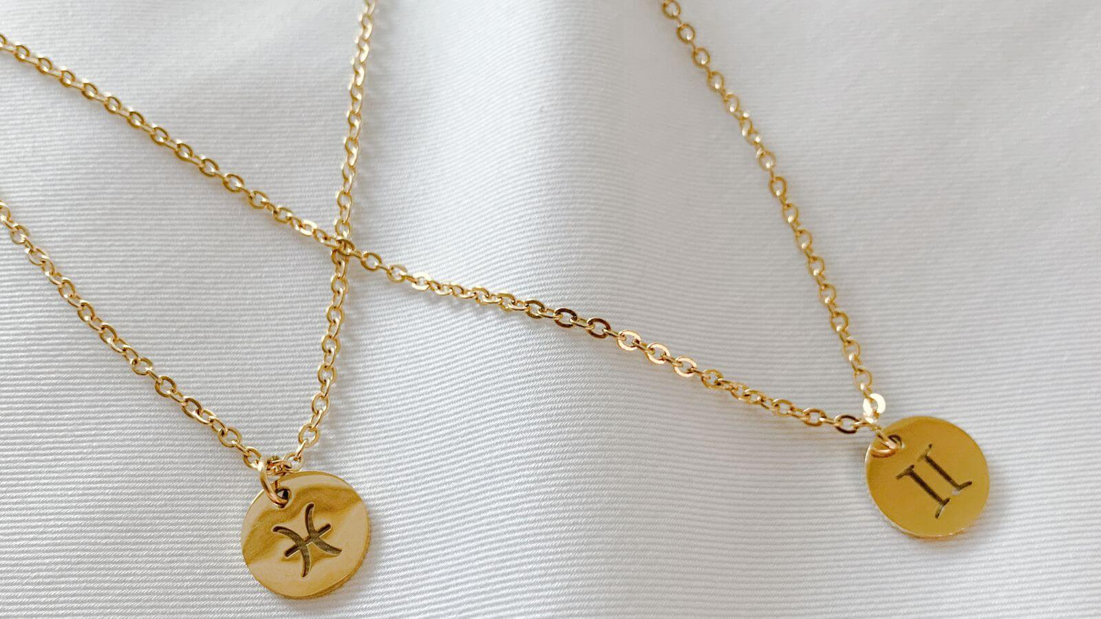 two gold necklaces with zodiac symbols